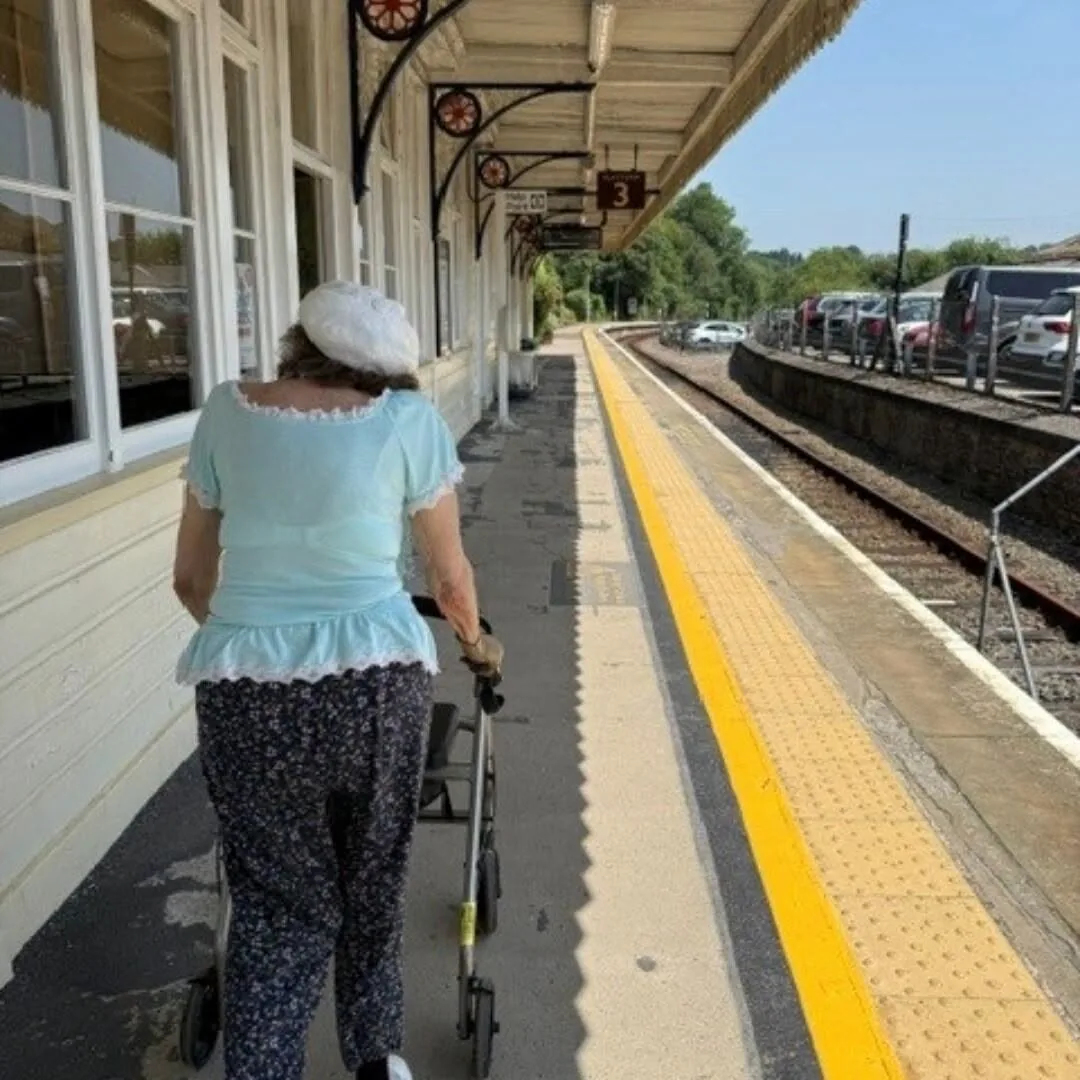Hazel walking along Looe railway station platform with her wheeled walking aid