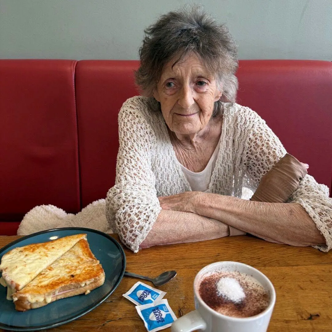 Hazel sitting at a café table with a toasted sandwich and a cup of coffee