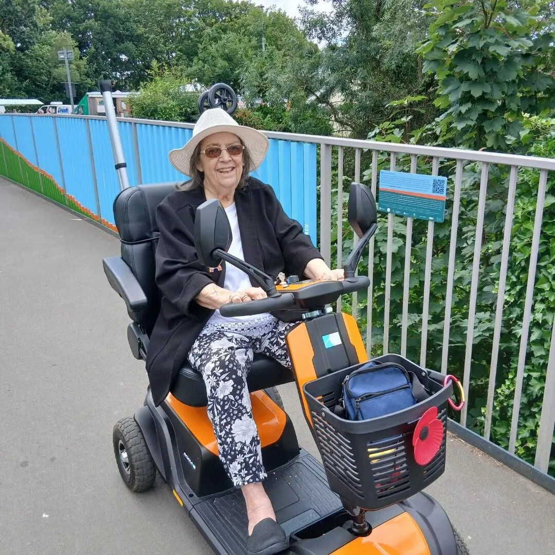 Pat smiling on her mobility scooter during a supported community outing